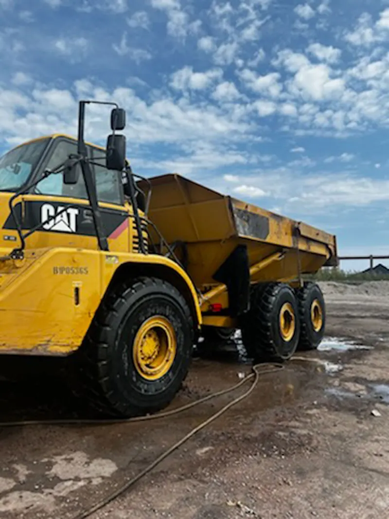 A crew member rinsing an articulated haul truck on site